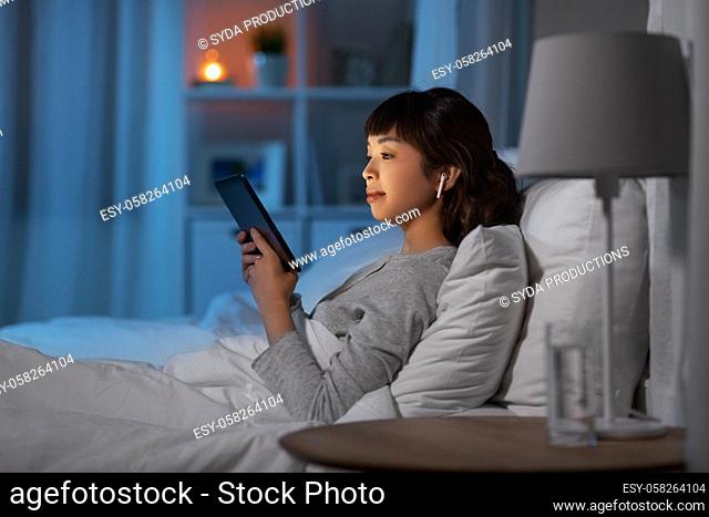 woman with tablet pc in earphones in bed at night