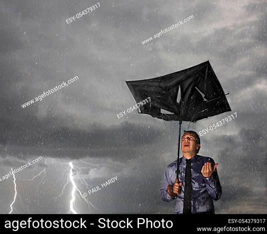 Businessman caught in a storm holding a broken umbrella