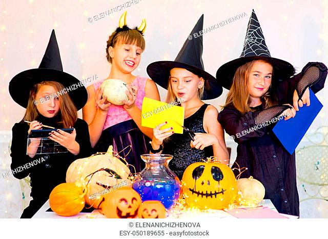 Happy group of teenagers in costumes preparing for Halloween, playing around the table with pumpkins and bottle of potion