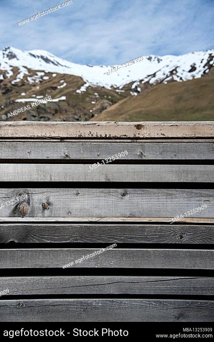 faded, gray wooden fence in front of the snow-covered range of hills near San Bernardino, Switzerland