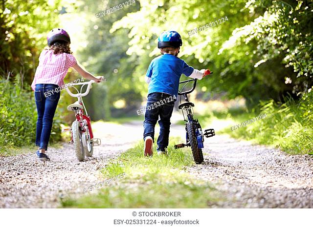 Two Children Pushing Bikes Along Country Track