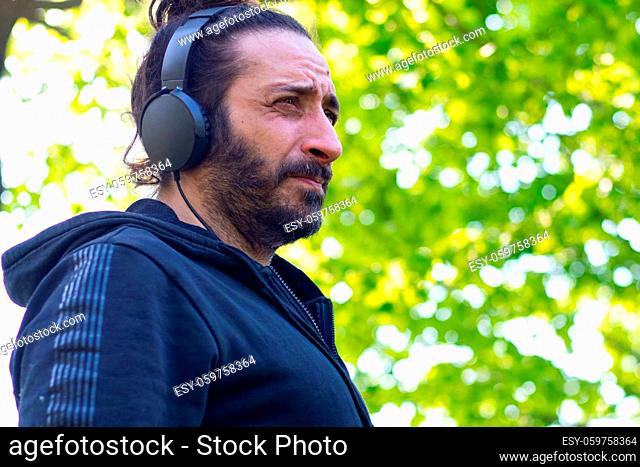 Hippy man with beard and headphones listening music outdoors on the garden. High quality photo