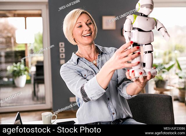Cheerful female entrepreneur examining robot model while working at home