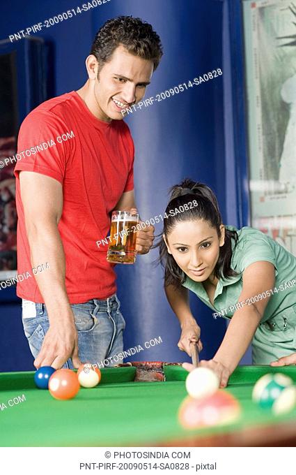 Young woman playing pool and a young man watching her game