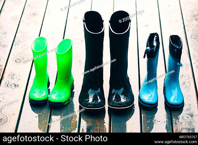 Row of wellies in various sizes standing on a wooden porch while raining