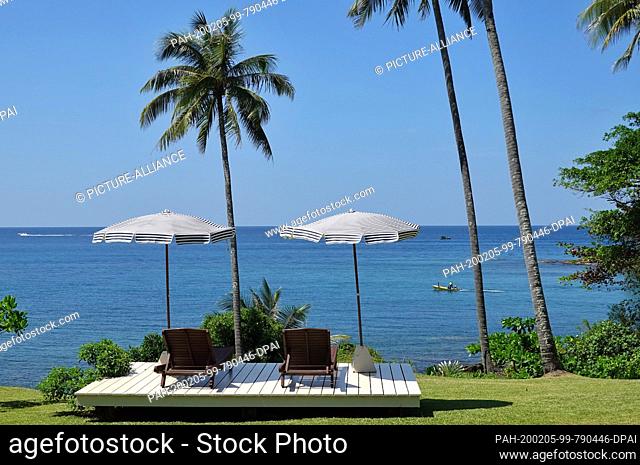30 October 2019, Thailand, Ko Kood: Deck chairs and parasols of Shantaa Resort Koh Kood under palm trees on a green meadow above the sea at the Gulf of Thailand