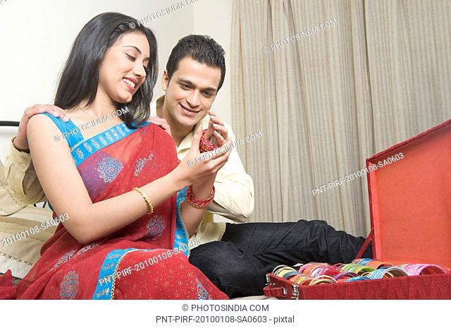 Woman putting on bangles with her husband sitting beside her