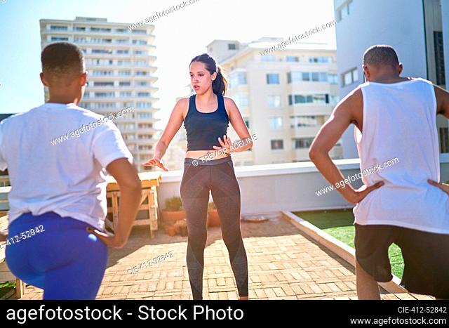 Young female yoga instructor teaching class on sunny urban rooftop