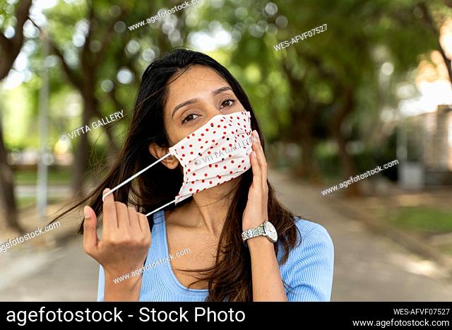 Beautiful woman wearing protective face mask in park during COVID-19