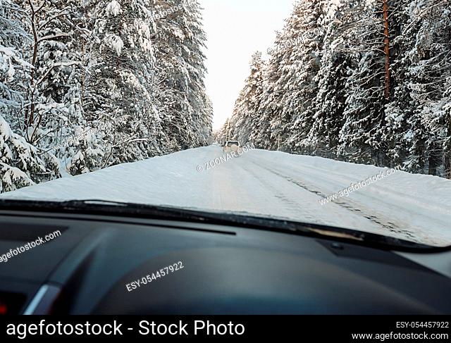 Passenger black car moving on winter road among deep forest shot from the driver s seat