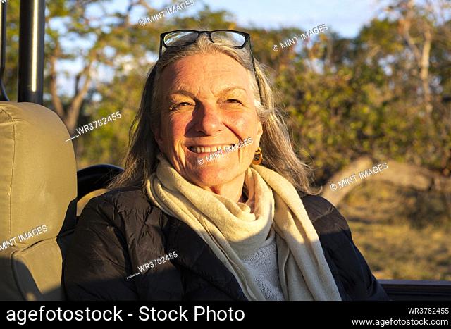 A smiling senior woman seated in a jeep at sunset, smiling