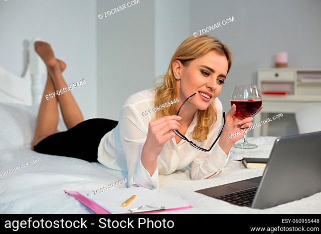 Woman making business in bed and having glass of red wine. Isolated on white background