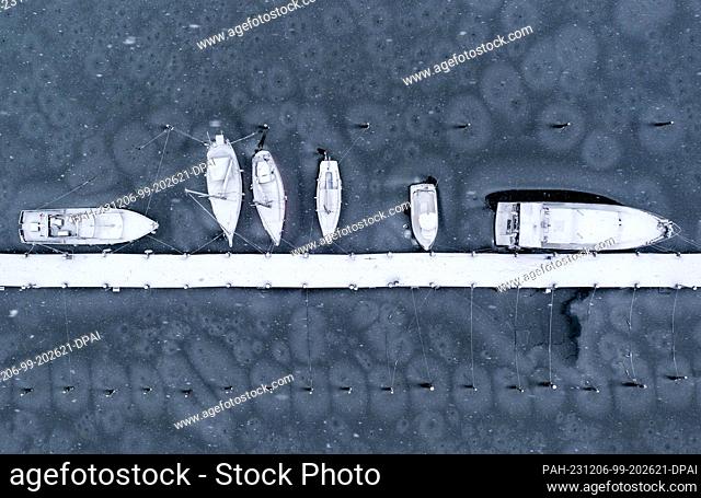 06 December 2023, Mecklenburg-Western Pomerania, Kirchdorf (poel): Boats covered in snow lie frozen in thin ice on a jetty in the harbor on the Baltic Sea...