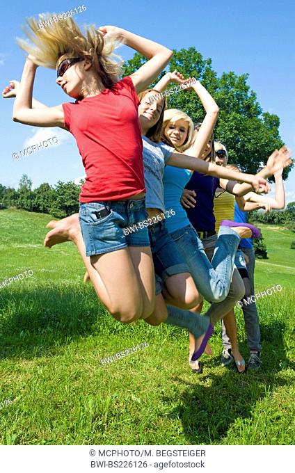 group of teenage girls in a meadow jumping into the air in a row behind each other
