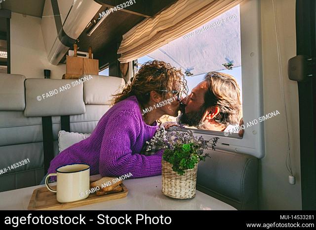 Romantic couple in love kissing during holiday vacation leisure. Woman sitting inside a modern camper kiss her husband outside it. People and vanlife