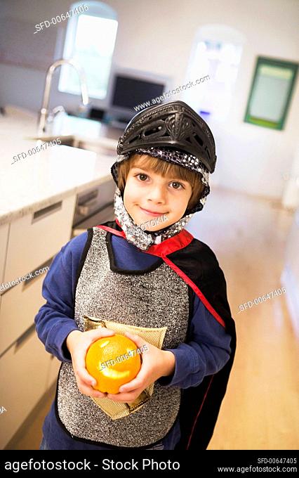 A Little Boy, Dressed as a Knight, Holding an Orange with a Face