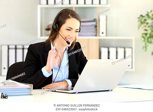 Happy telemarketer having a video conference with a laptop waving with her hand at office