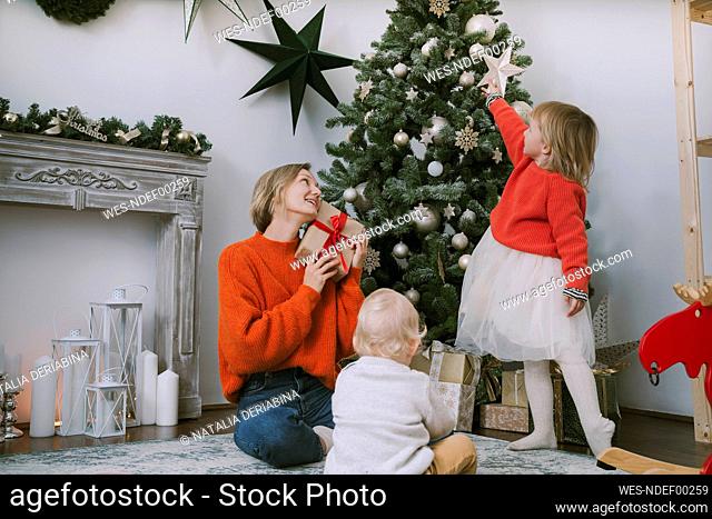 Mother and children sitting by Christmas tree at home
