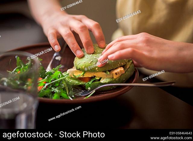 Picture of vegan dish represented on wooden plate. Lady's hands taking vegan burget from plate in vegan restaurant or cafe