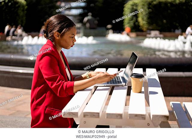 Businesswoman working on laptop outdoors, London, UK