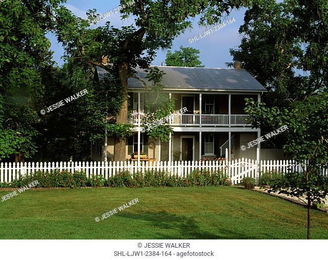 EXTERIORS: Two story home, white picket fence, porches on both levels run the length of the house