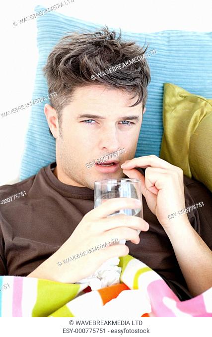 Diseased caucasian man taking pills with water lying on the sofa