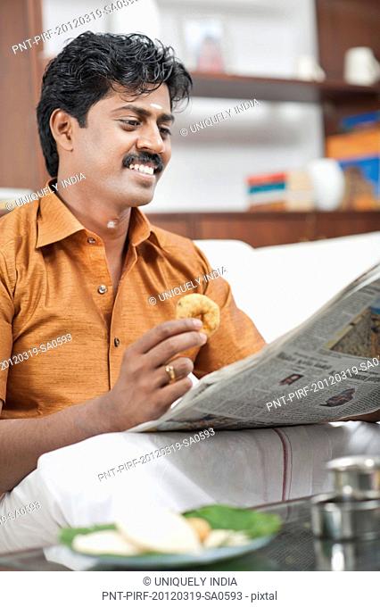South Indian man reading a newspaper and having breakfast