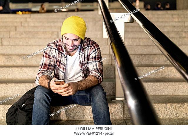 UK, London, man sitting on a staircase and looking at his phone on a night commute