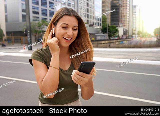 Excited young woman touching her wireless earphones to turn them on and to listening favorite music outdoors