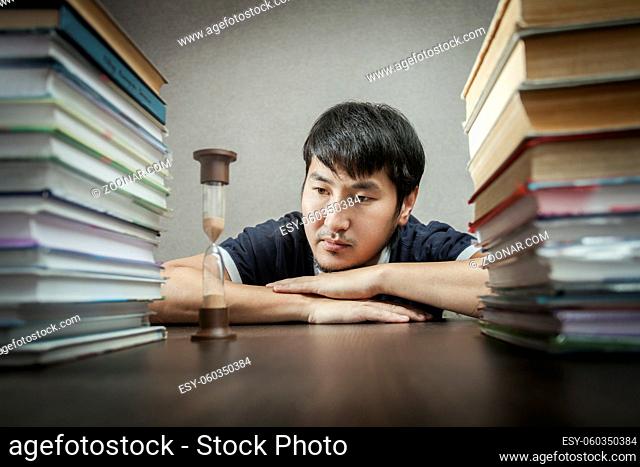 The young man looks at hourglasses lying on a table between textbooks