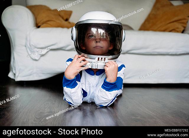Thoughtful girl wearing space costume and helmet lying on floor at home