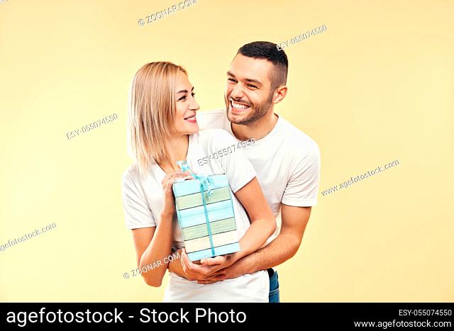 Young happy couple with gift box over beige background. Present, holiday, celebration concept