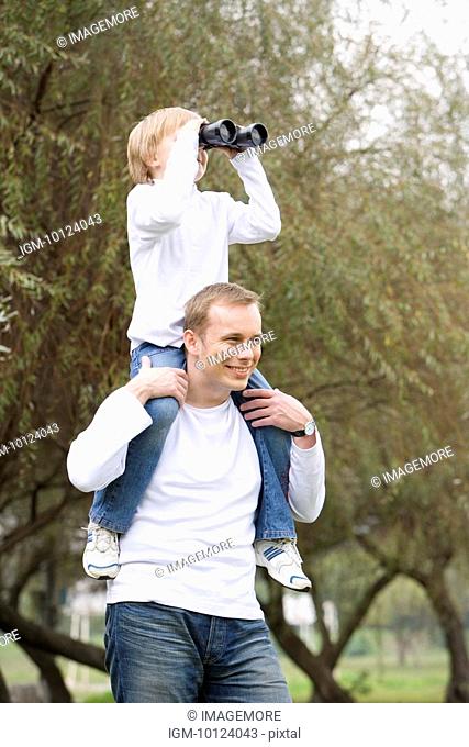 Father carrying son on shoulders, looking through binoculars
