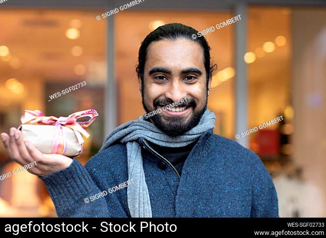 Close-up of smiling young man showing Christmas present against building