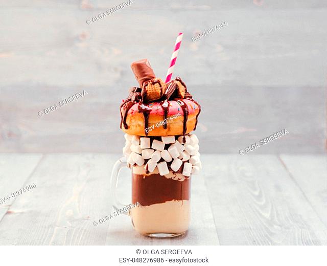 Chocolate and donuts extreme milkshake with marshmallow and other sweets in mason jar on gray wooden background. Crazy freakshake on gray wooden table with copy...