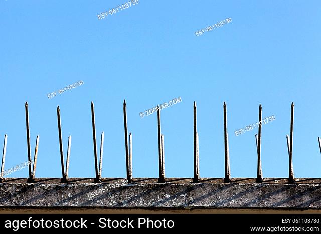 old brick fence on top of which metal spikes are installed to protect the territory, against the background of the blue sky, close-up and details