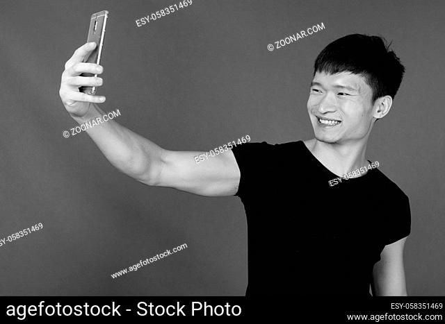 Studio shot of young Chinese man wearing black shirt against gray background in black and white