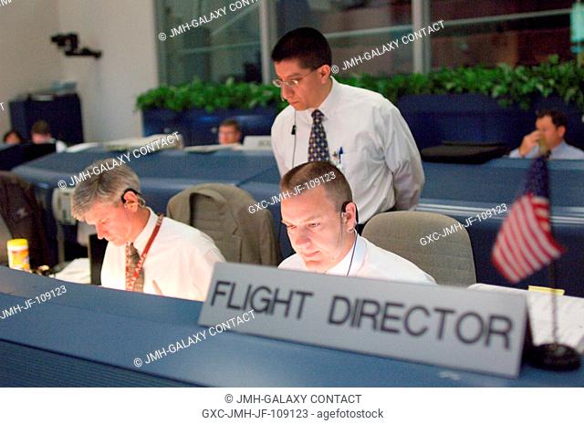 Flight directors Bryan Lunney (left), Richard Jones (standing) and Norm Knight monitor data at their consoles in the space shuttle flight control room of...
