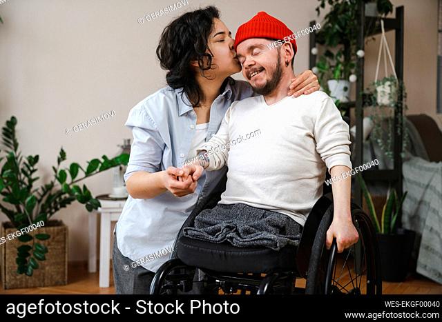 Woman kissing boyfriend with disability on head at home