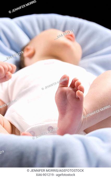 A newborn baby dressed in a white bodysuit lies on a blue blanket  The angle is from his feet