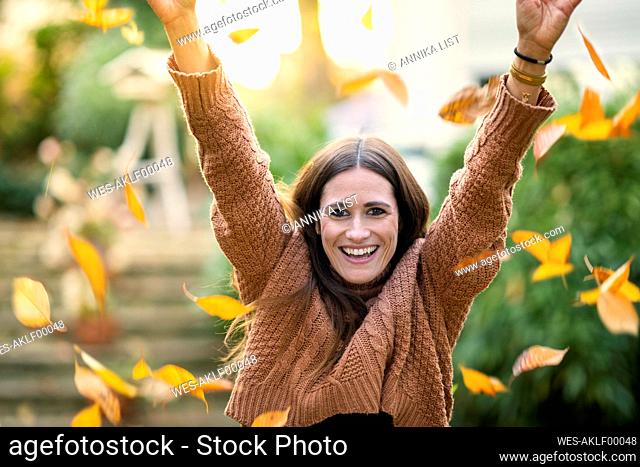 Cheerful woman throwing leaves during autumn