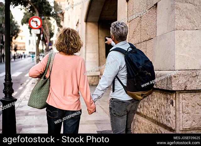 Mature couple holding hands walking on footpath at vacation