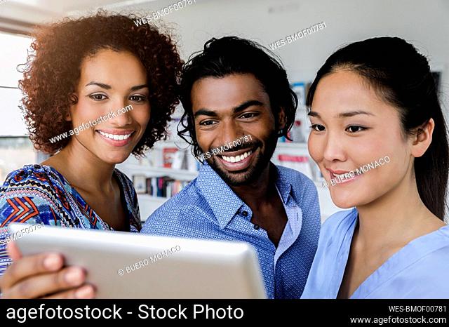 Smiling businessman with female colleagues looking at tablet while discussing in office
