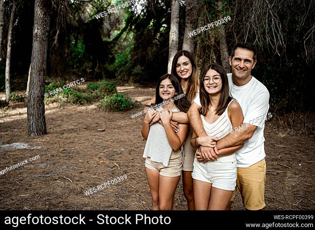 Mother and father embracing daughters while standing in forest