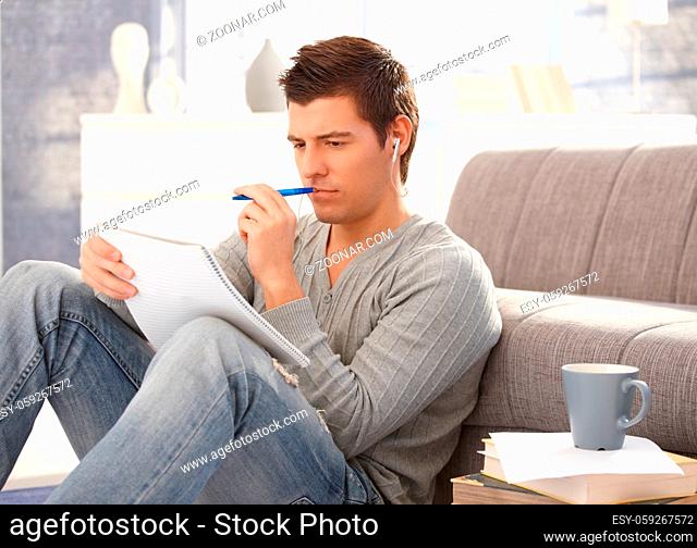 Concentrating university student guy sitting on floor, learning at home