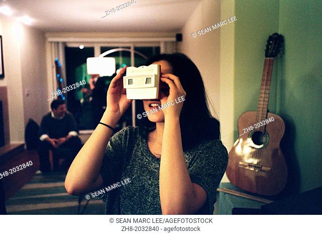A young woman enthusiastically peers through a view-master type toy in a studio in Los Angeles