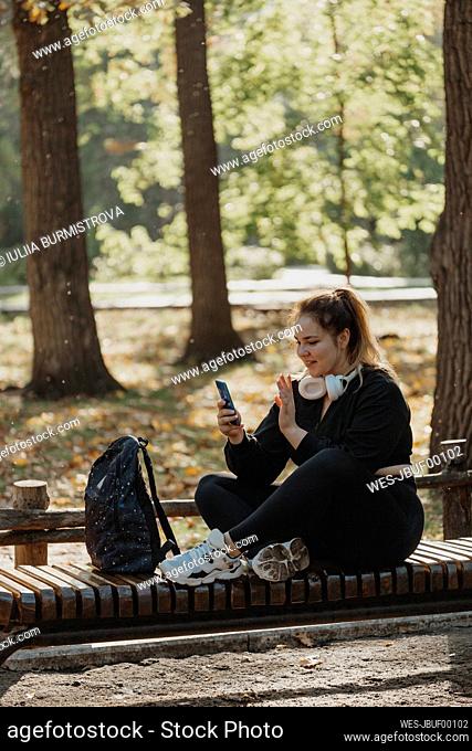 Smiling woman having video call through smart phone on bench in park