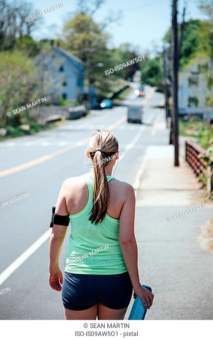 Rear view of woman wearing activity tracker carrying water bottle walking along road