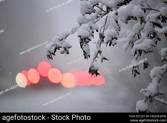 01 December 2023, Baden-Württemberg, Stuttgart: Taillights of vehicles shine in the morning rush hour traffic on a road through a snow-covered wooded area in...
