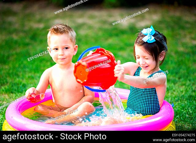 Subject childhood summer games in the yard. Caucasian brother and sister playing plastic toys bucket sitting in the water, inflatable round children's pool